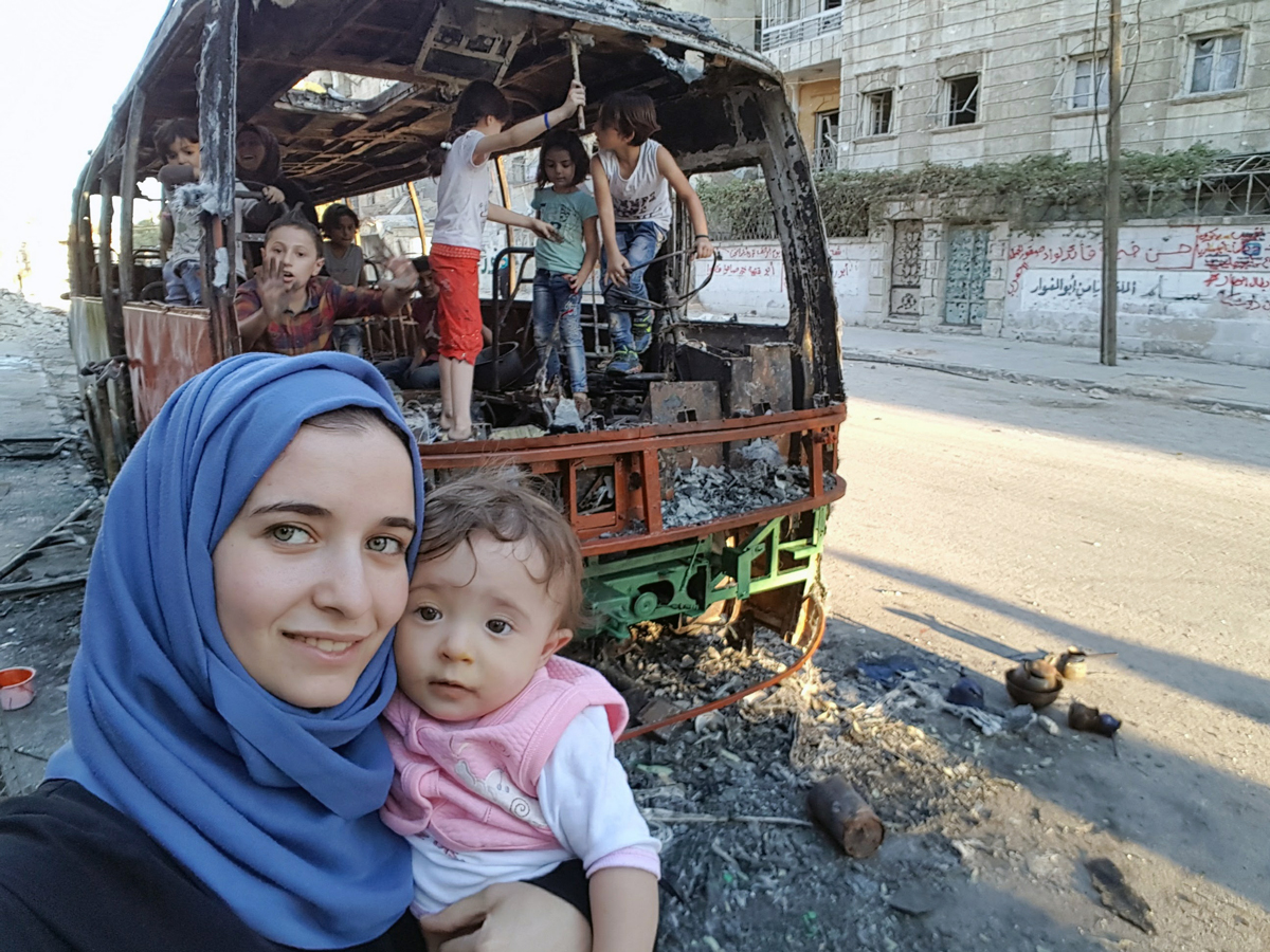 Waad Al-Kateab s dcerou v Aleppu, za nimi vypálený autobus