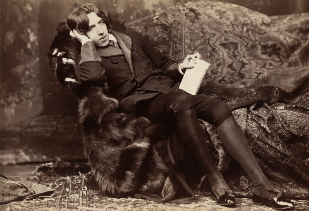 Oscar Wilde lenoší v pohovce, u nohou má psa