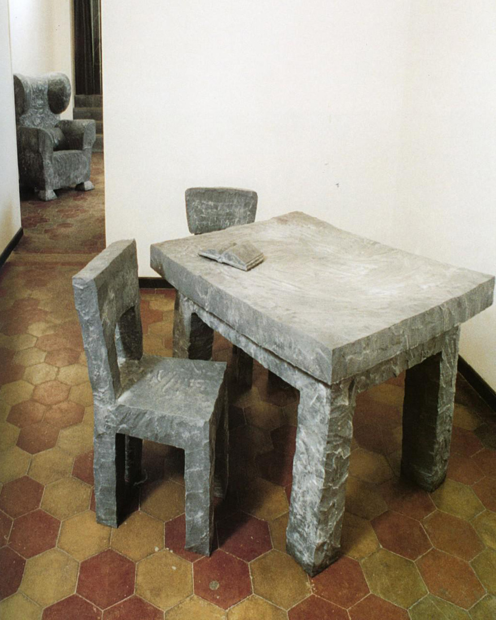 stůl s rozloženou knihou, dvě židle, v pozadí křeslo