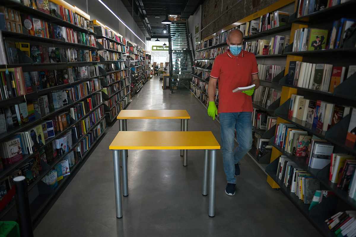 pracovník knihkupectví s rouškou kráčí uličkou mezi regály