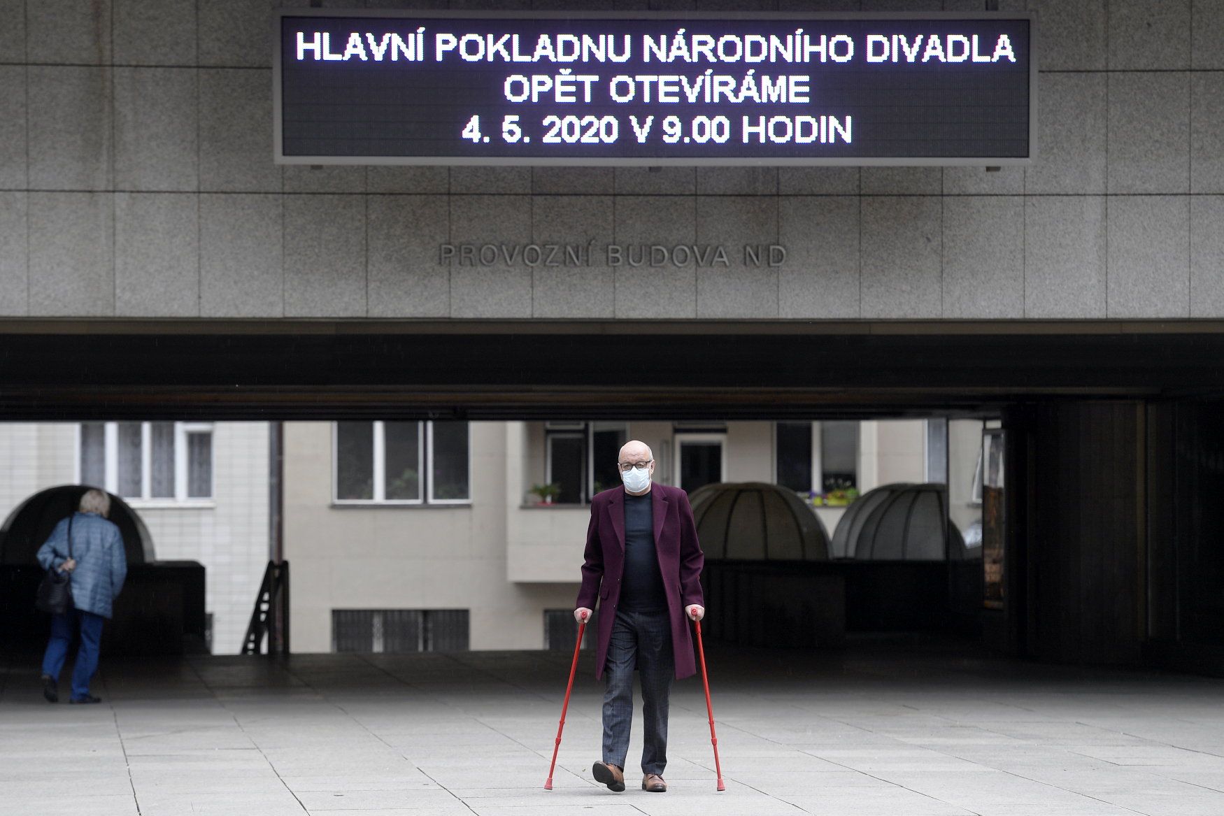 Muž s nasazenou rouškou prochází 4. května 2020 piazzetou Národního divadla