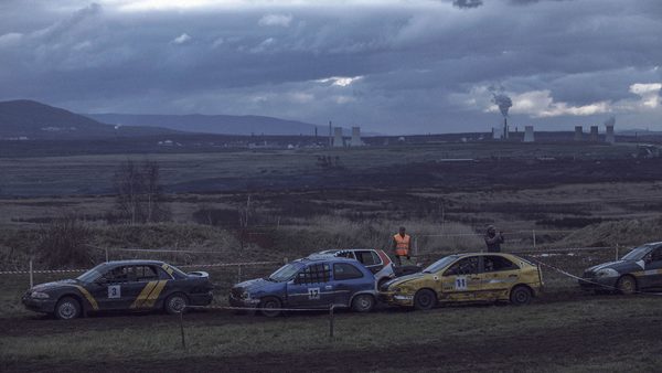 amatérský automobilový závod na louce, v pozadí kouřící továrny