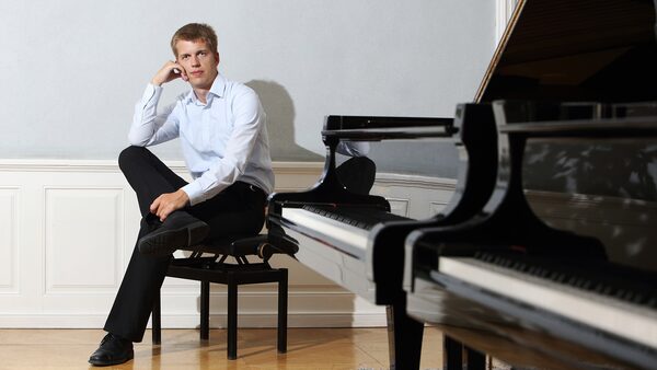 Marek Kozák sedí na klavírní židličce, v popředí klavír