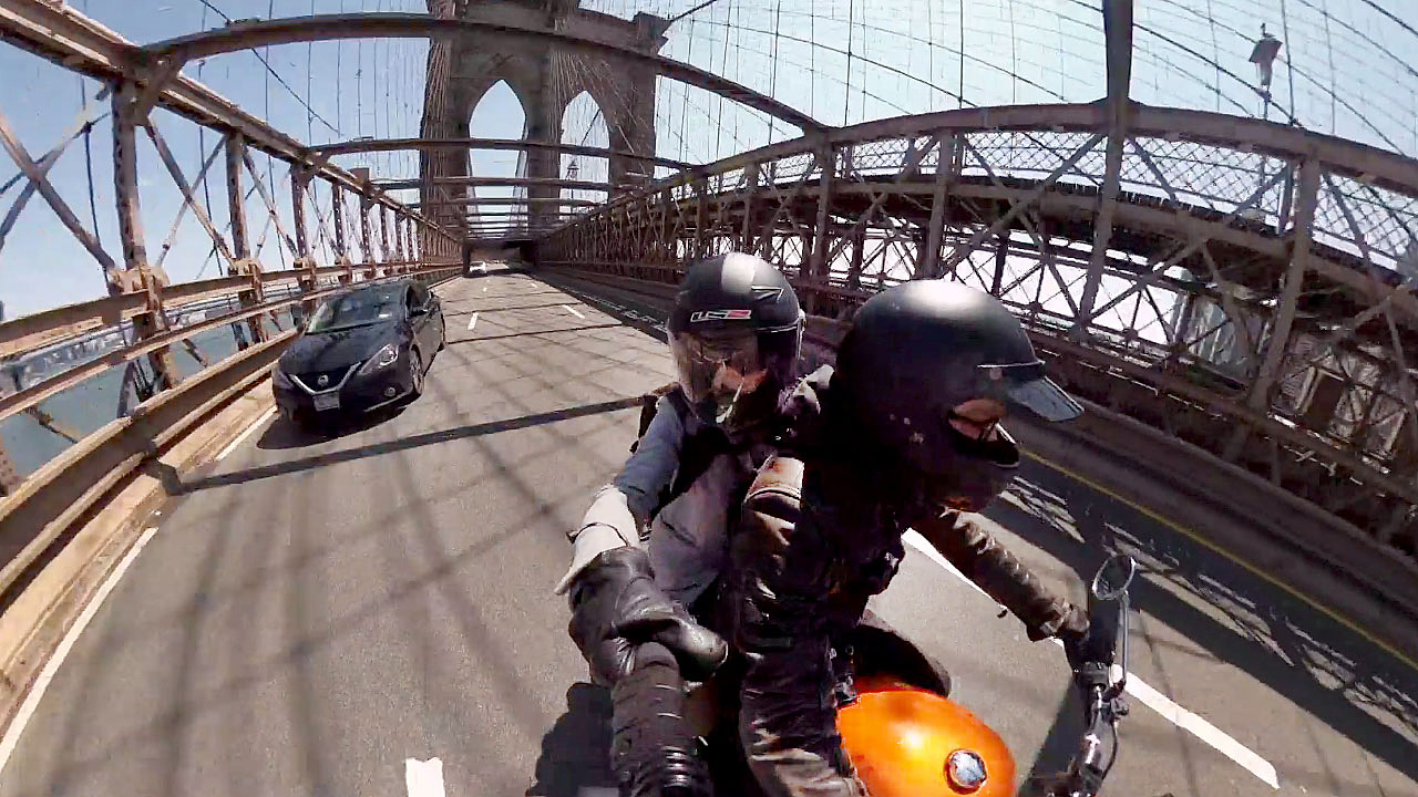 dvojice na motorce projíždí po mostě
