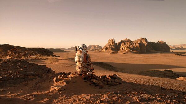 muž v kosmonautském oděvu sedí na poušti