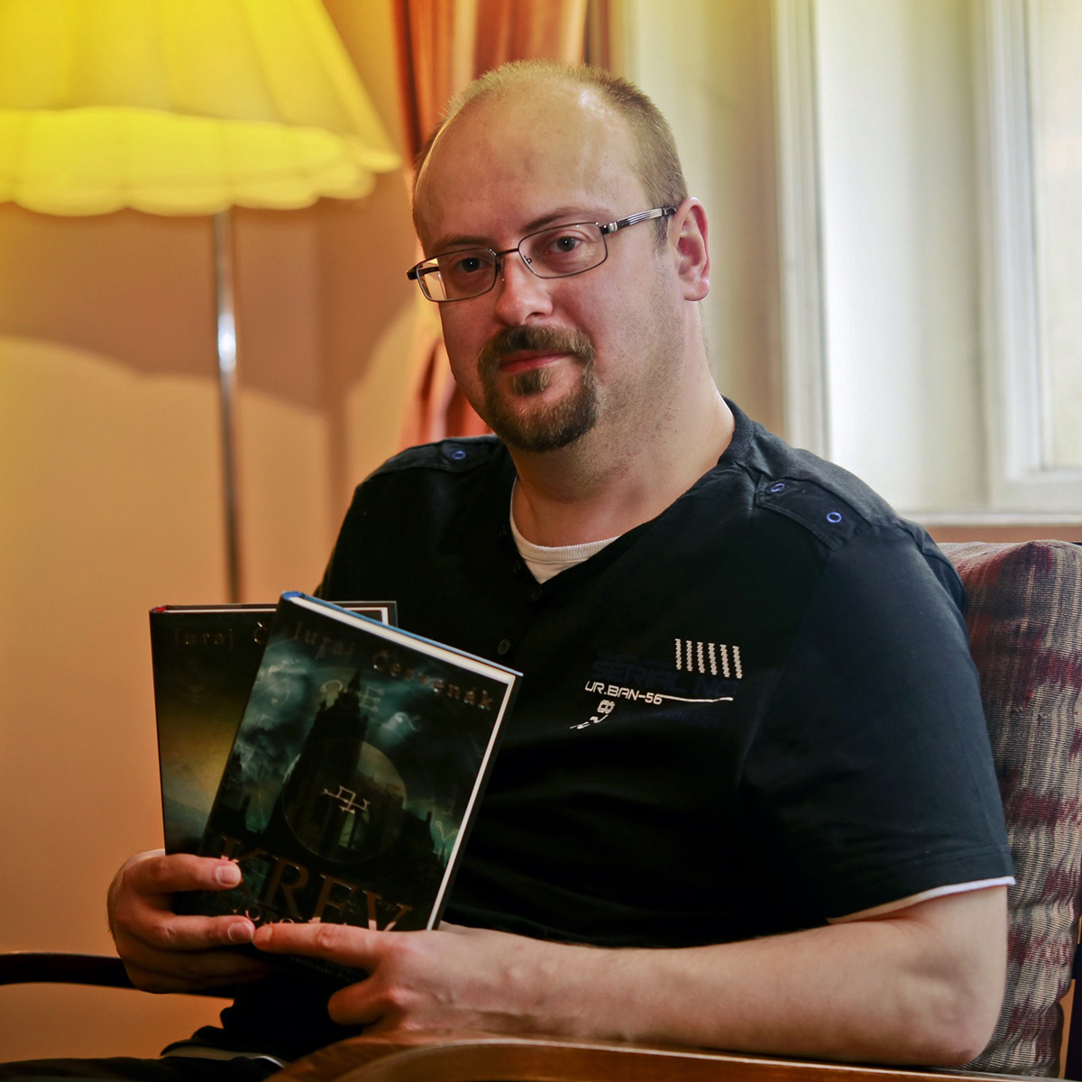 Juraj Červenák pózuje v křesle se dvěma svými knihami