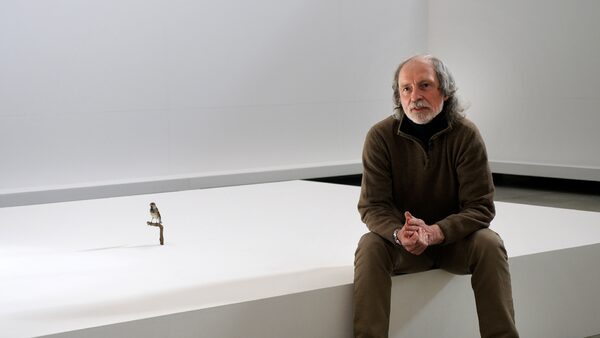 Jiří Kovanda sedí na galerijním soklu, v pozadí vycpaný vrabec