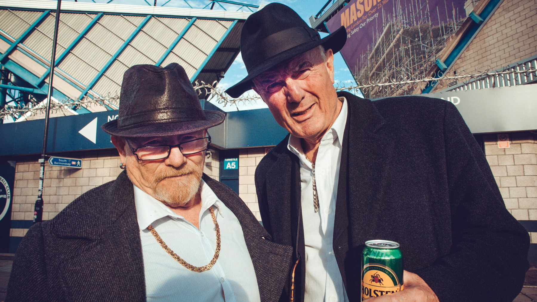 dva muži s klobouky před fotbalovým stadionem