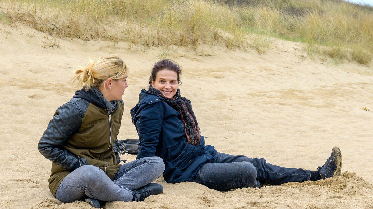 dvě ženy v bundách sedí a hovoří na pláží