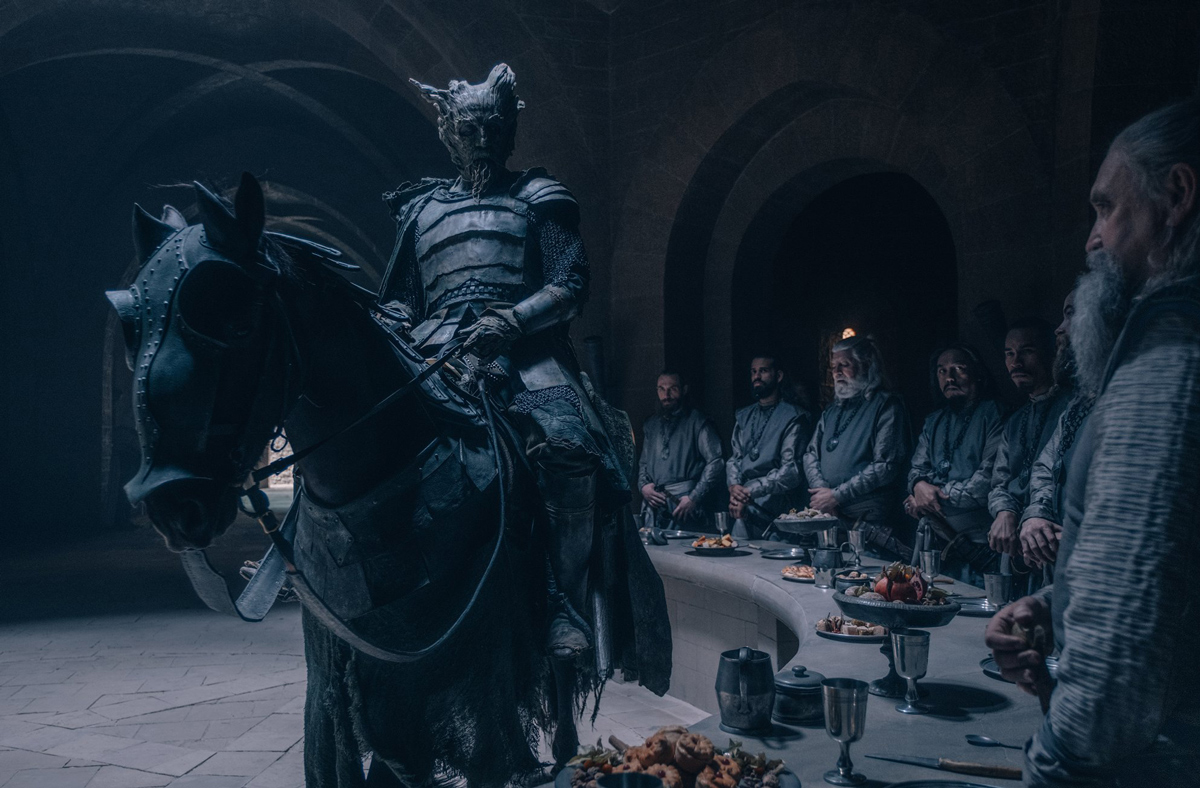 rytíř na koni v sále s prostřeným kulatým stolem a za ním stojící další rytíři