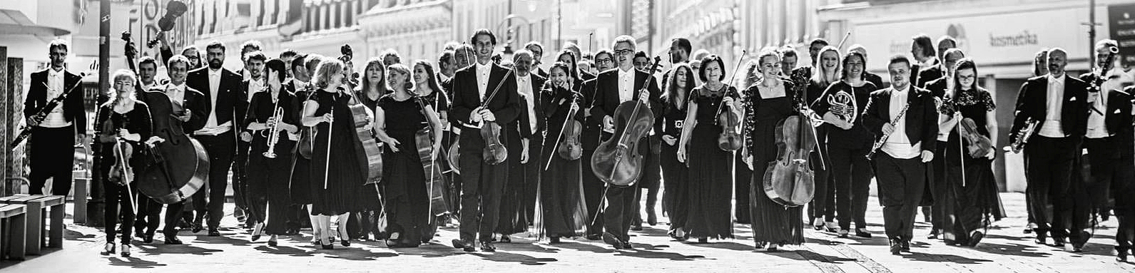 členové a členky orchestru s nástroji jdou městem