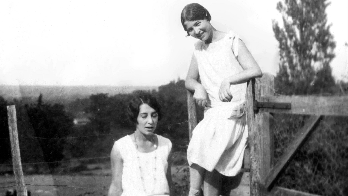 dvě dívky v bílých šatech pózují u ohrady