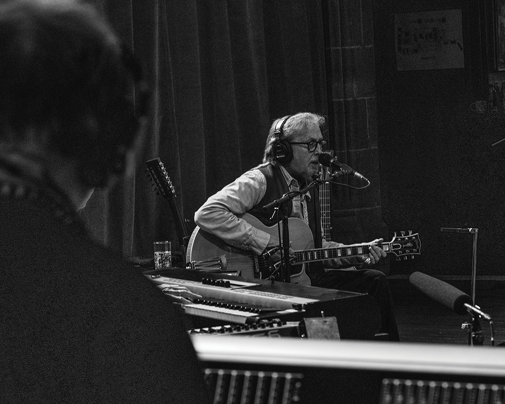 Černobílé foto hudebníka Erica Claptona za mikrofonem s kytarou