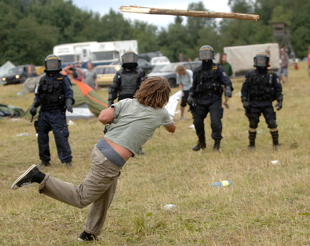 Jeden z příznivců techna hází klacek na postupující policisty, kteří 30. července 2005 za asistence vodních děl, dýmovnic a slzného plynu zakročili na loukách u Mlýnce na Tachovsku proti účastníkům technoparty CzechTek. Foto: ČTK – Petr Eret