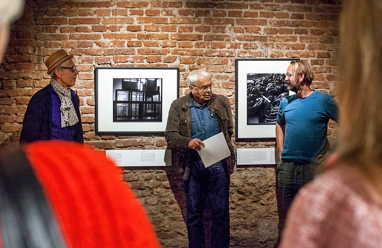 vernisáž, v popředí tři muži, za nimi fotografie