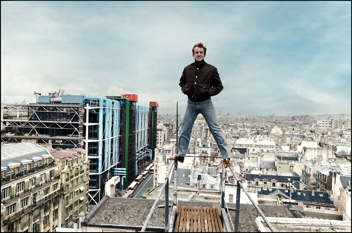 Jean-Paul Belmondo stojí na zábradlí, v pozadí Paříž